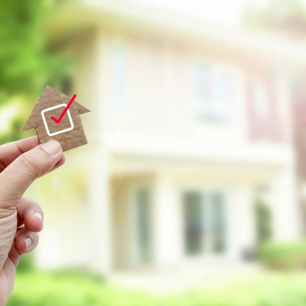 Person holding a tiny home with a checkmark in front of a house