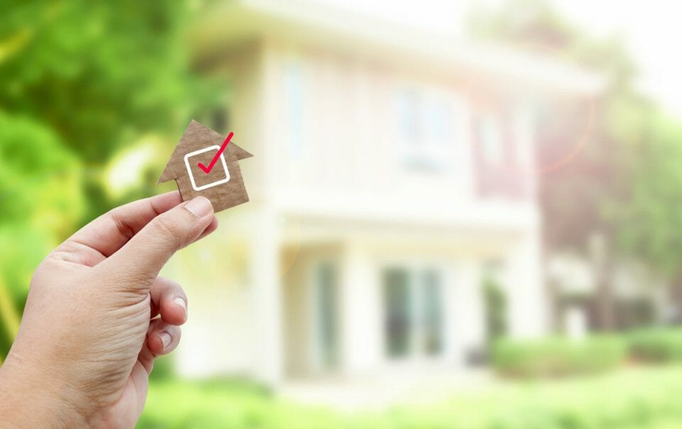 Person holding a tiny home with a checkmark in front of a house